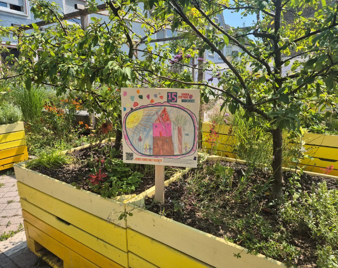 Die Kinderzeichnung als Schild in einem Pflanzenkübel im Trapp Areal.