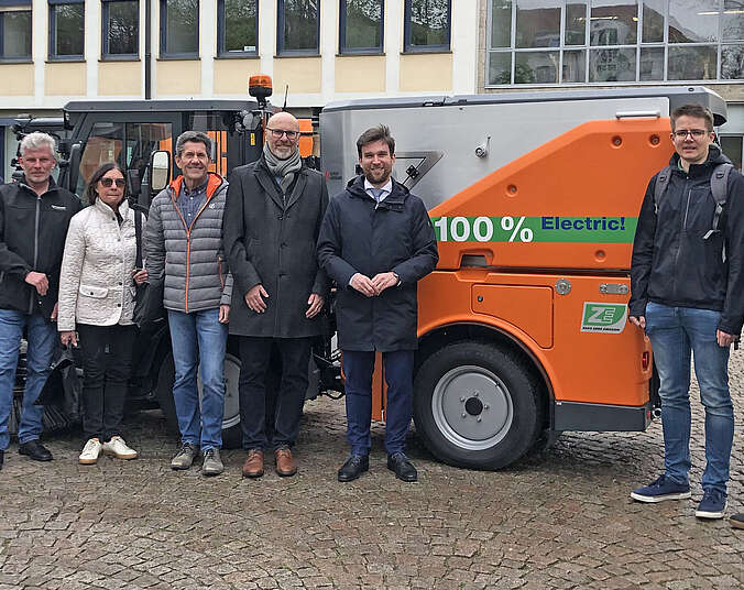 Männer und eine Frau stehen vor einer orangefarbenen E-Kehrmaschine