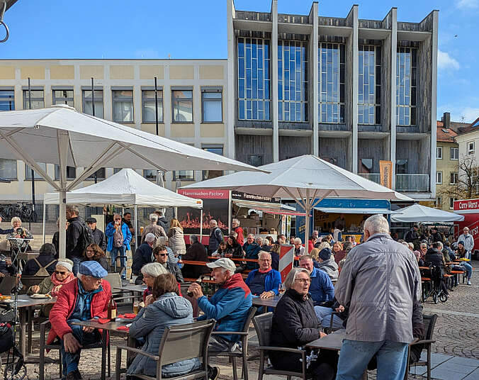 Menschen sitzen an Biertischen unter Sonnenschirmen