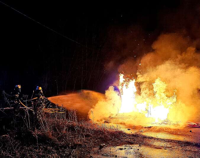 Einsatzkraft der Feuerwehr hält Löschschlauch in der Hand und löscht loderndes Feuer