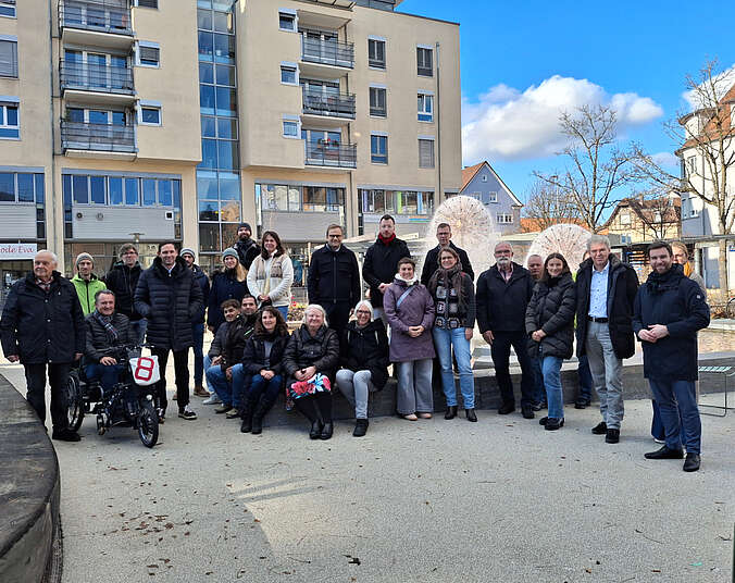 Männer und Frauen stehen vor einem Brunnen