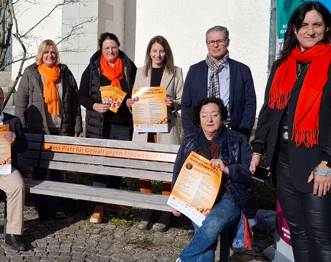 Frauen und Männer sitzen auf der Bank bzw. stehen hinter der Bank