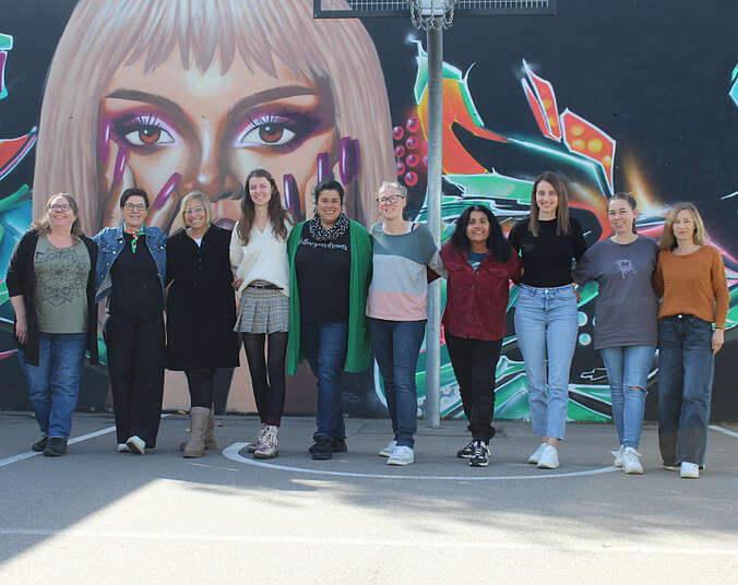 Frauen stehen vor einem großen Graffiti-Bild mit einem Gesicht..